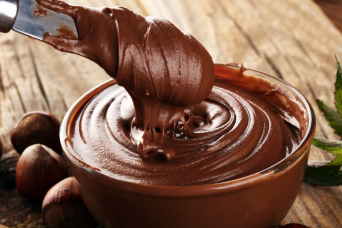 ciotola di vetro piena di crema spalmabile al cacao con intorno delle nocciole