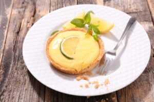 crostata su un piatto con accanto delle fette di limone, delle foglioline di menta e una forchetta