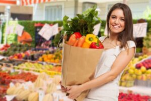 donna sorridente al supermercato che tiene una borsa piena di ortaggi