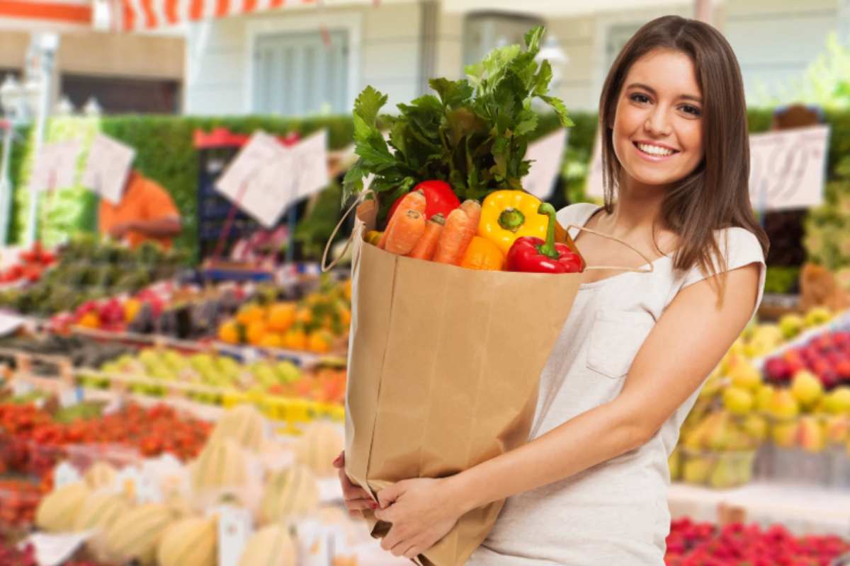 donna sorridente al supermercato che tiene una borsa piena di ortaggi