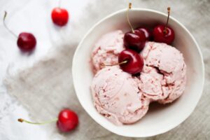 tre palline di gelato dentro ad una tazza con sopra delle ciliegie