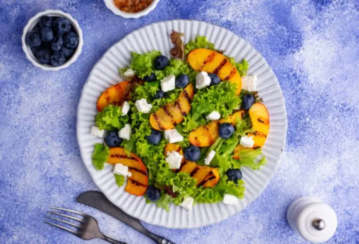 insalatona mista con pesche e mirtilli dentro ad un piatto e accanto delle ciotoline