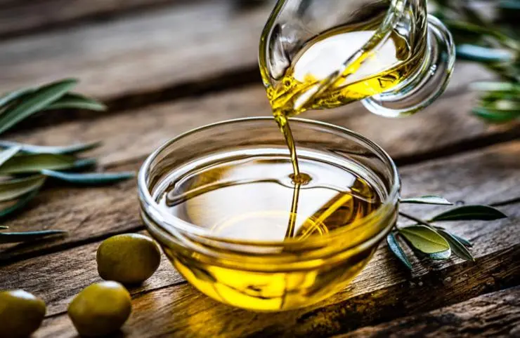 persona che versa dell'olio dentro ad una ciotola di vetro e intorno delle olive