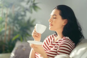 donna seduta sul divano che beve un caffè con gli occhi chiusi