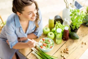 donna appoggiata ad un tavolo su cui c'è un insalata, degli ortaggi e dei succhi di frutta