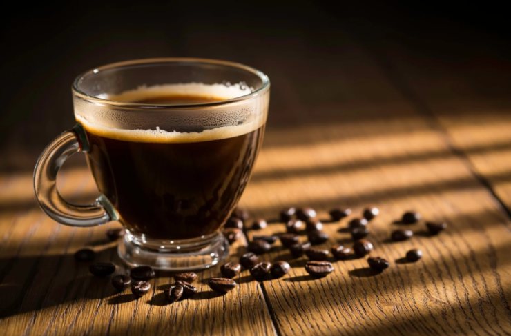 tazzina di caffè circondata da chicchi di caffè
