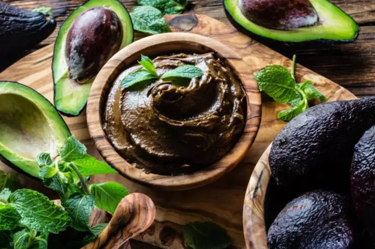 mousse al cacao dentro ad una tazza di legno con intorno degli avocado e delle foglie di menta