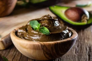 mousse al cacao dentro ad una coppa di legno con sopra delle foglie di mente e dietro mezzo avocado