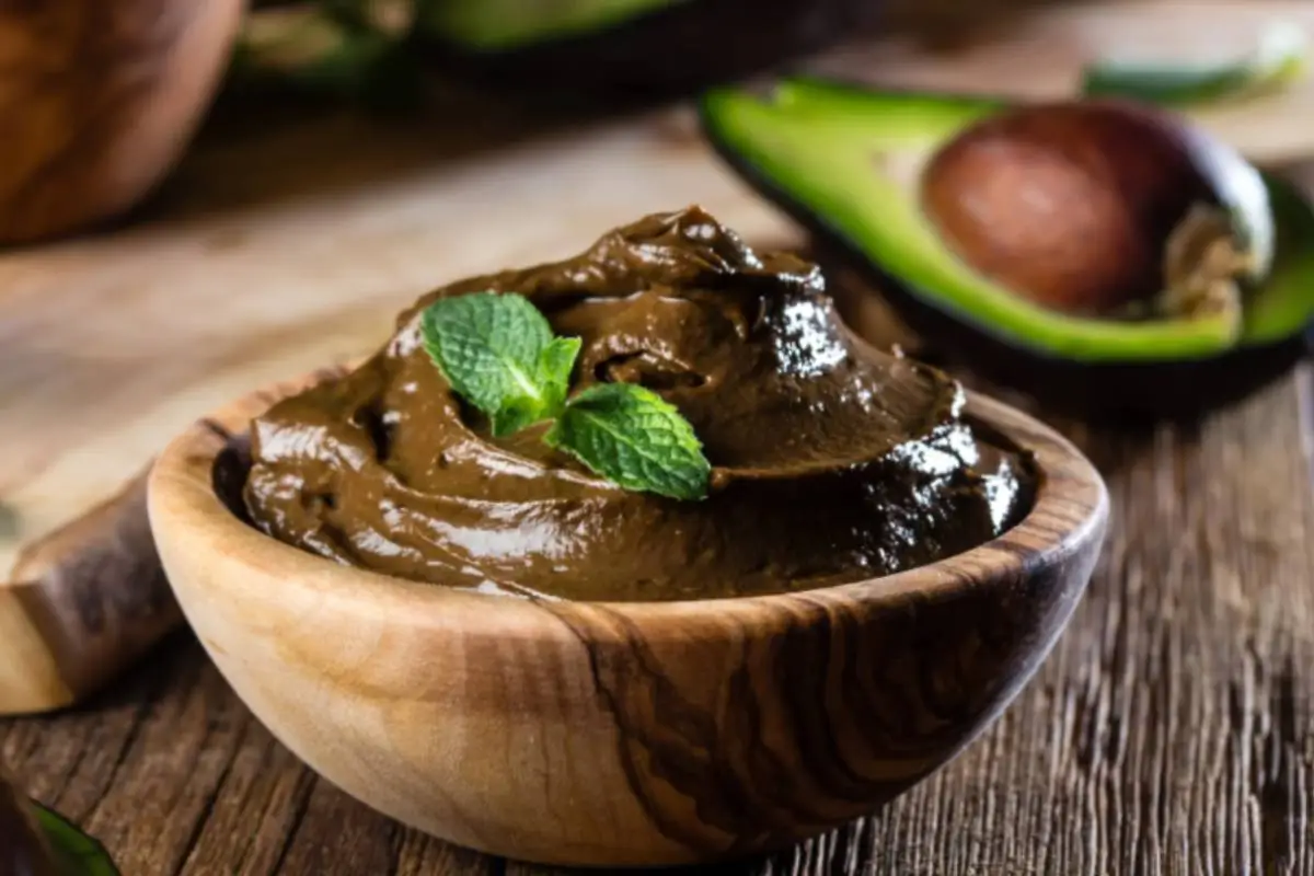 mousse al cacao dentro ad una coppa di legno con sopra delle foglie di mente e dietro mezzo avocado