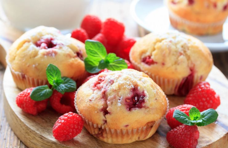 tre muffin sopra ad un tagliere circondati da lamponi e foglie di menta