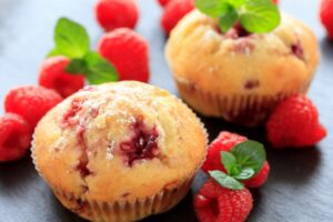 due muffin ai lamponi con intorno dei lamponi freschi e delle foglie di menta
