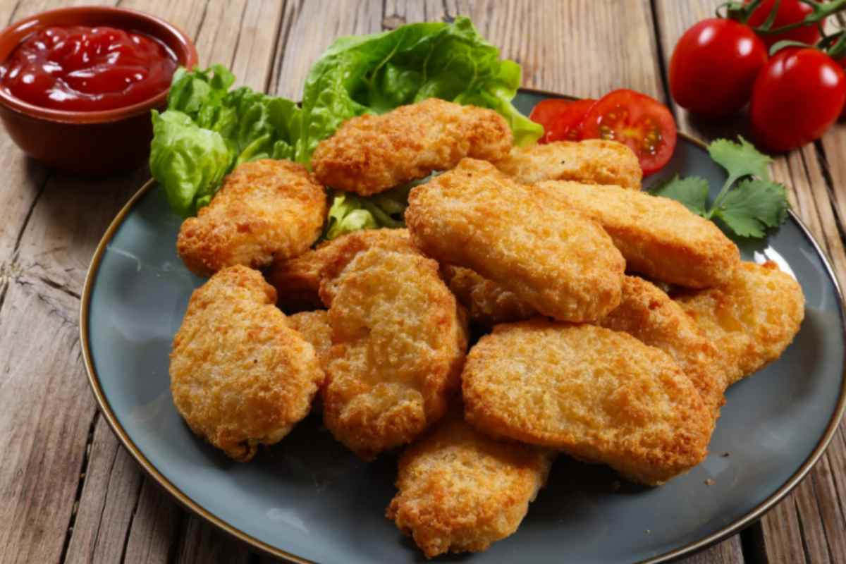 nuggets su un piatto con accanto insalata pomodori e una ciotolina con dentro una salsa rossa