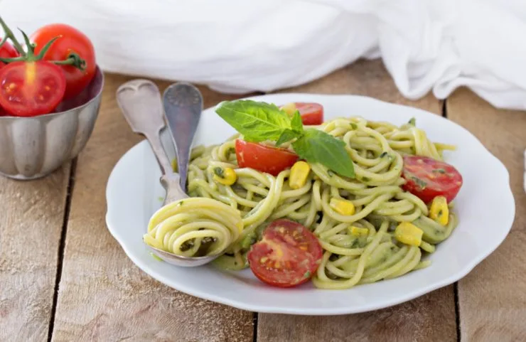 spaghetti con pesto pomodorini e mais e accanto delle posate appoggiate sul piatto