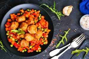polpette e verdurine in un piatto con accanto uno spicchio di aglio e delle posate
