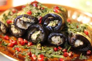 involtini di melanzane su un piatto con intorno foglie di menta e chicchi di melograno