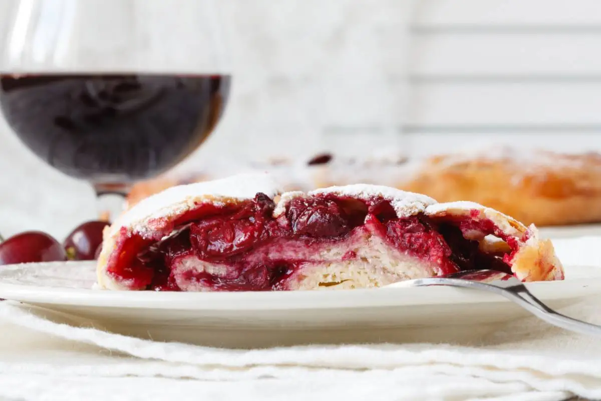 Fetta di crostata all'amarena e bicchiere di vino rosso
