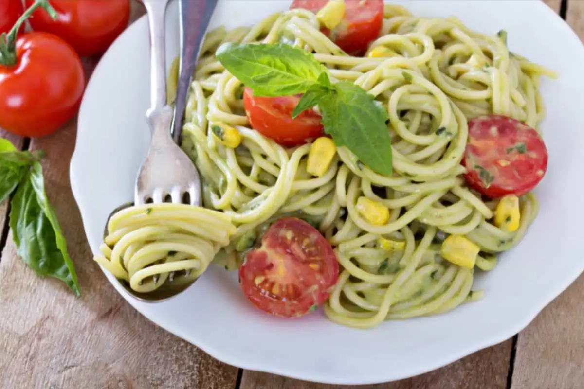 spaghetti con pesto pomodorini e mais e accanto delle posate appoggiate sul piatto