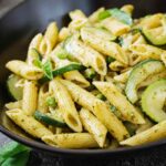 pasta con zucchine pisellini e foglie di menta dentro ad un piatto nero