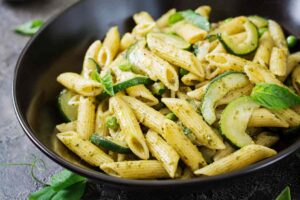 pasta con zucchine pisellini e foglie di menta dentro ad un piatto nero