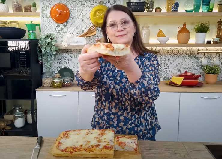 una donna con della pizza in teglia e una fetta in mano