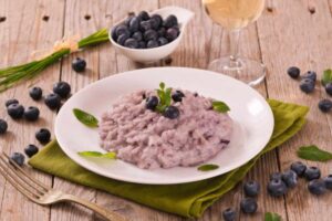 risotto ai mirtilli con accanto mirtilli un bicchiere di vino e una forchetta
