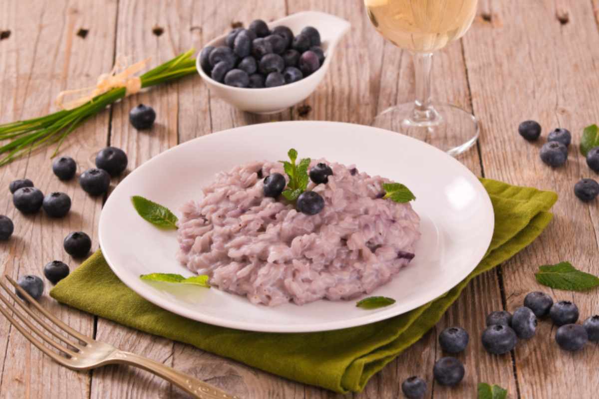 risotto ai mirtilli con accanto mirtilli un bicchiere di vino e una forchetta