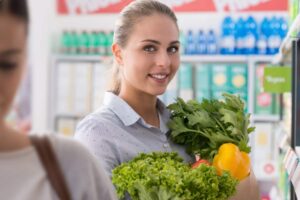 ragazza sorridente al supermercato con in mano delle buste piene di ortaggi