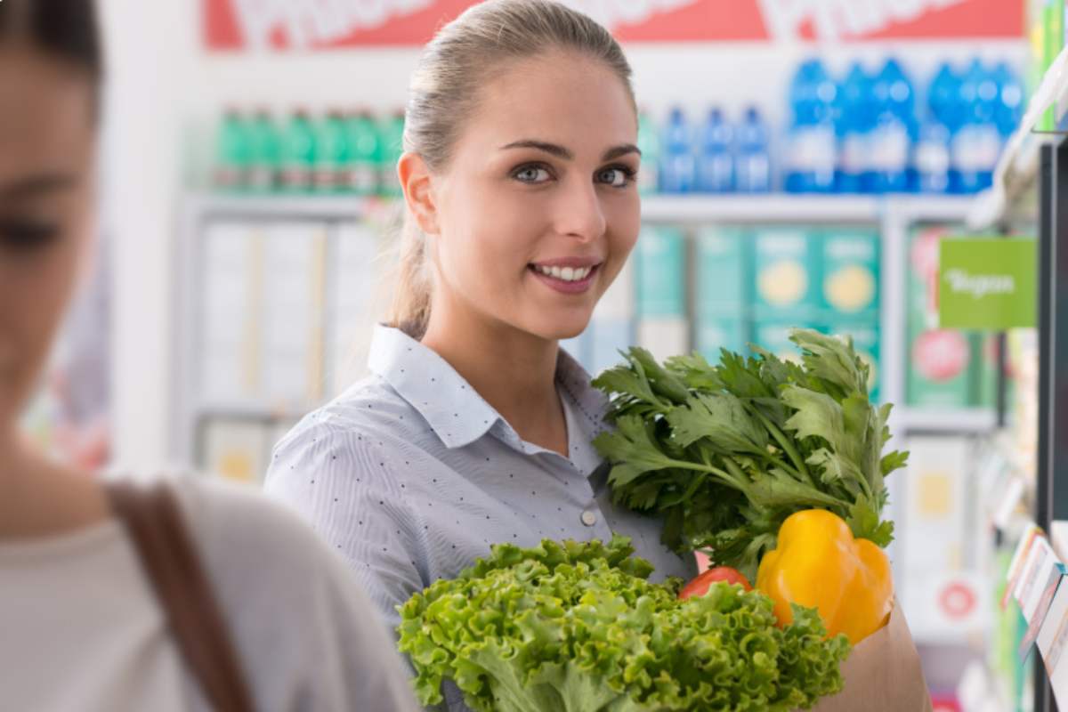 ragazza sorridente al supermercato con in mano delle buste piene di ortaggi