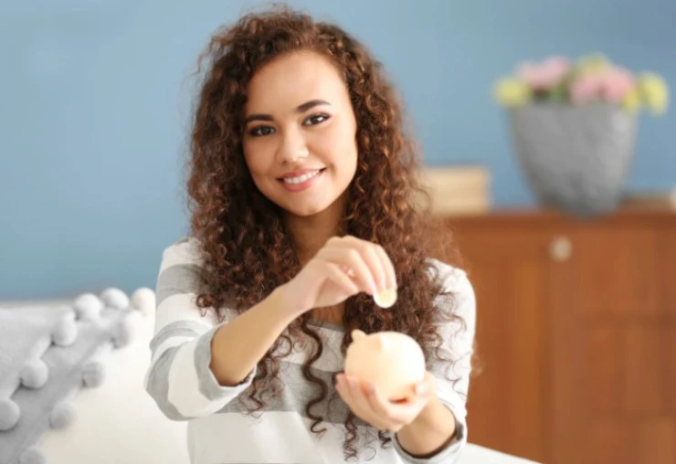 ragazza che sorride mentre mette una moneta dentro ad un salvadanaio che tiene in mano