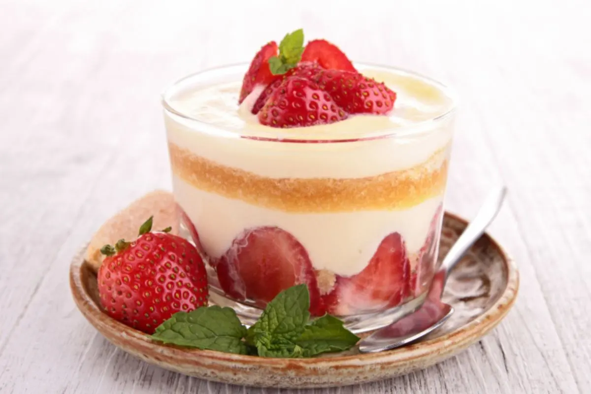 coppetta di tiramisù alle fragole con intorno delle fragole e della menta fresca