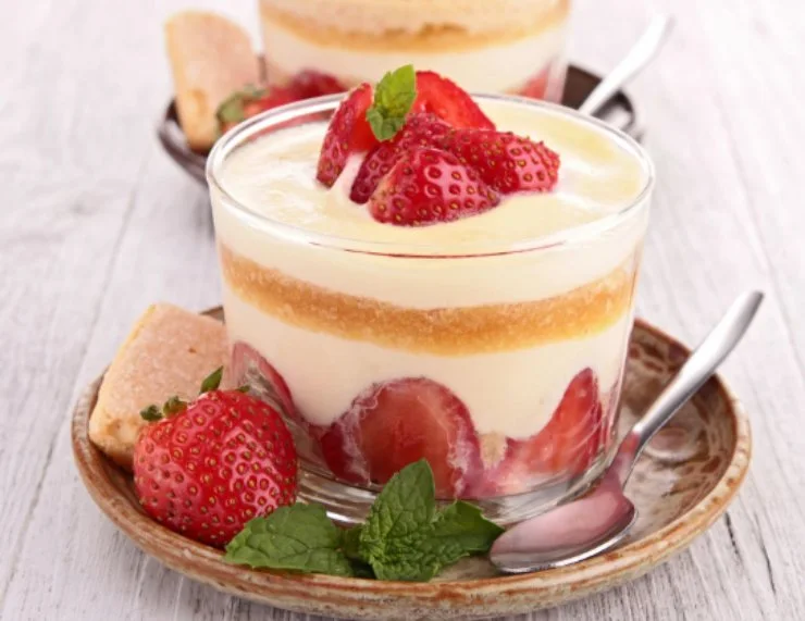 due coppette di vetro piene di tiramisù alle fragole su un piattino con accanto un cucchiaino