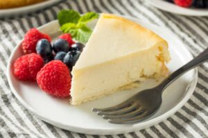 fetta di torta su un piatto con accanto fragole, mirtilli e foglie di menta e una forchetta