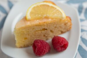 fetta di torta su un piatto con sopra una fettina di limone e accanto dei lamponi