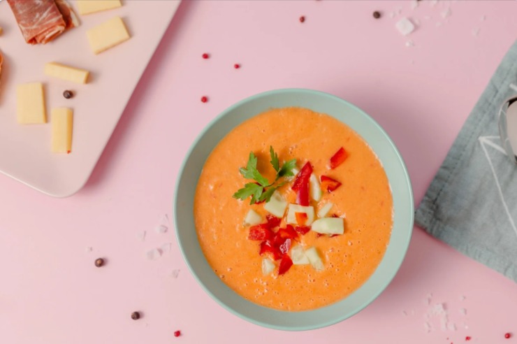 zuppa nel piatto con sopra delle verdurine e accanto un tagliere con salumi e formaggi