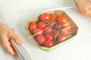 Donna che mette pellicola trasparente sui pomodori
