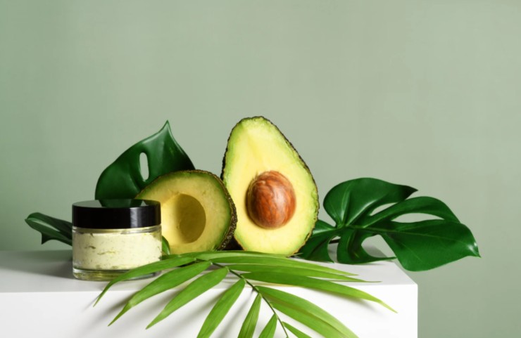 avocado tagliato a metà foglie di piante e vasetto di crema