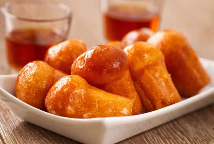 piatto con babà al rum e bicchieri con il rum sullo sfondo