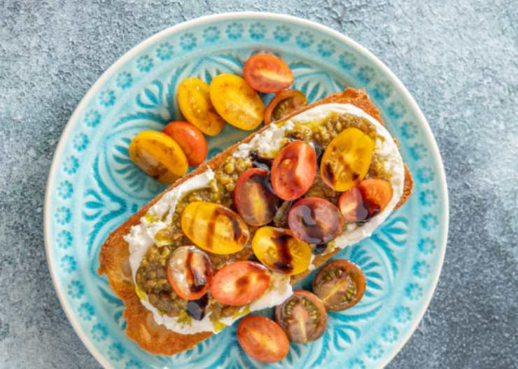 bruschetta con pesto formaggio e pomodorini e accanto dei pomodorini 