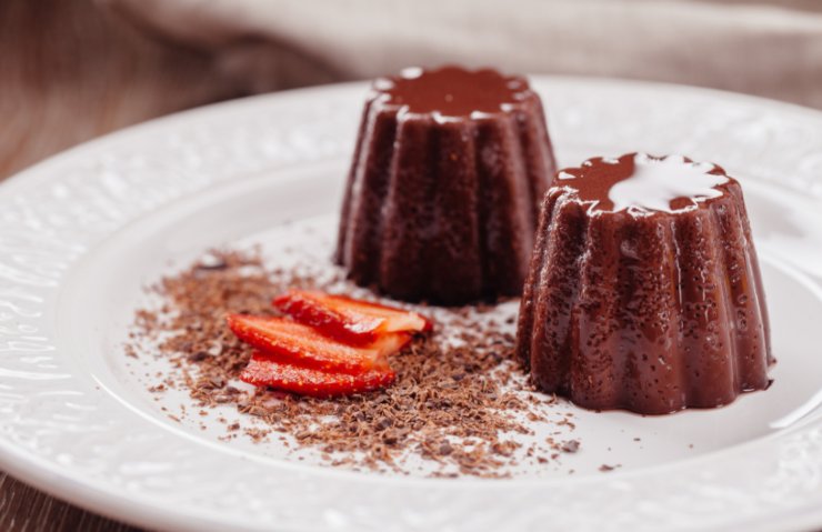 due budini al cioccolato su un piatto con accanto delle fragole