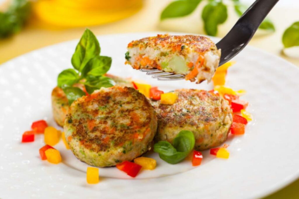 burger di verdure su un piatto circondati da pezzetti di peperoni e foglie di basilico