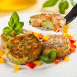 burger di verdure su un piatto circondati da pezzetti di peperoni e foglie di basilico