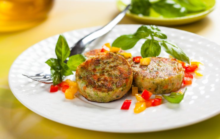 burger vegetali in un piatto con peperoni e basilico e accanto una forchetta