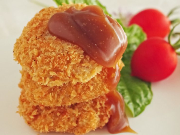 cotolette con sopra della salsa e accanto dei pomodori