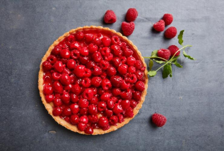 crostata ricoperta di lamponi con intorno dei lamponi freschi