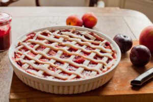 crostata con la marmellata dentro alla teglia e intorno delle prugne