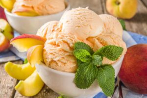 gelato alla pesca dentro ad una coppa con intorno delle pesche