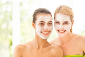 due amiche che sorridono con la maschera di bellezza in faccia