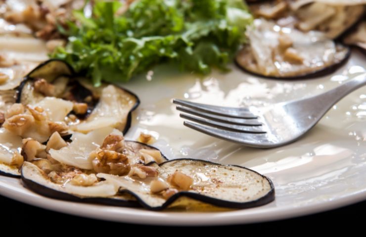melanzane grigliate su piatto con dell'insalata e accanto una forchetta
