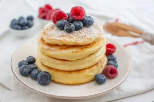 pancakes impilati su un piatto con sopra dei frutti di bosco