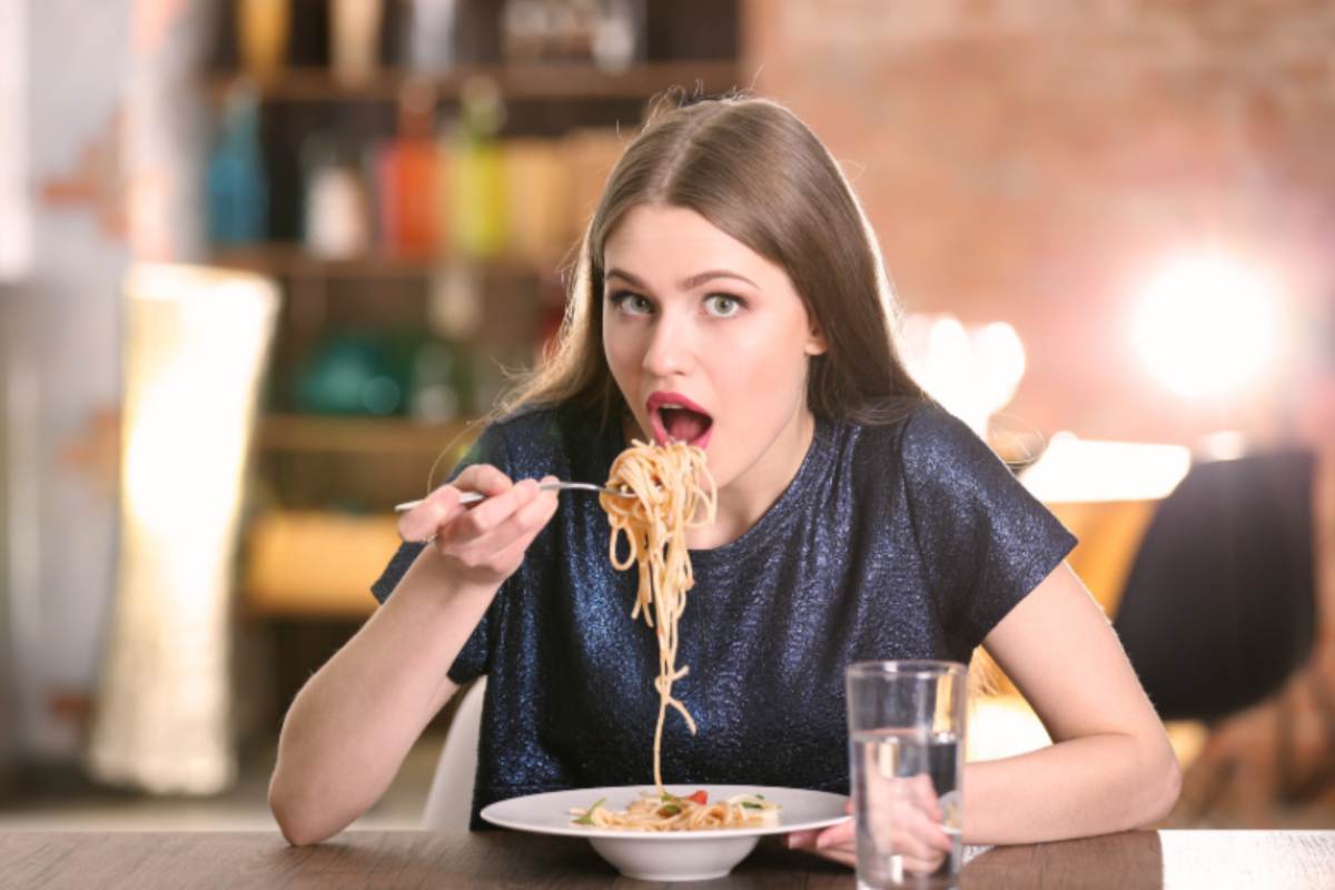 donna seduta al tavolo che mangia un piatto di spaghetti